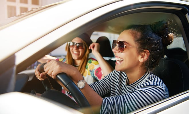 Two women with sunglasses smile and drive
