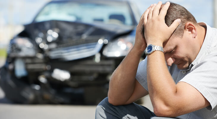 Stressed man with a damaged car in the background