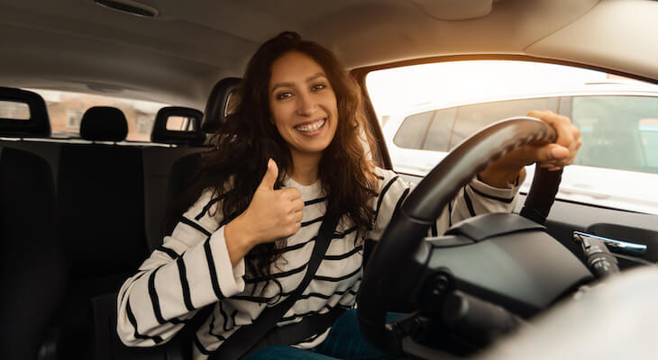 Kemper auto insurance: woman doing the thumbs up while driving a car