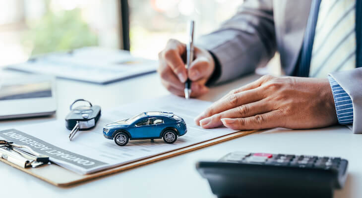 How long does it take to get car insurance: person signing a contract with a car key and a miniature car on it