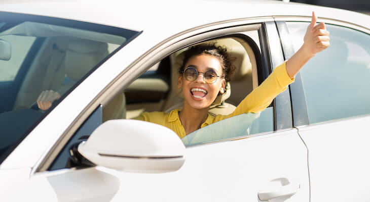 How to switch car insurance: Happy woman behind the wheel of her car giving a thumbs up