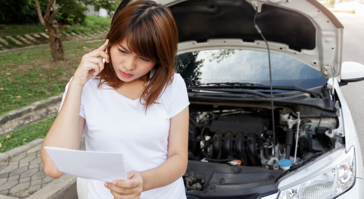 How to switch car insurance: Woman talking on the phone outside her car reading a document