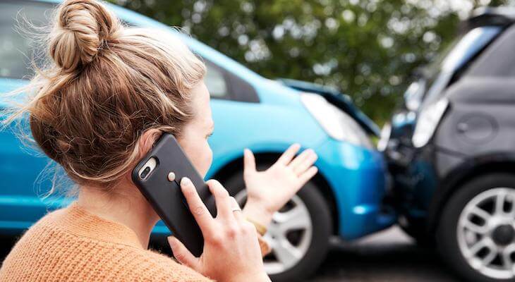 Woman talking on the phone while pointing at 2 cars that crashed into each other