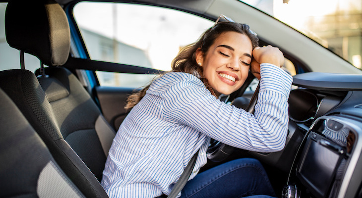 Woman happily hugging her car's steering wheel