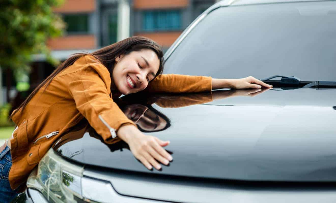 woman smiling while hugging her vehicle