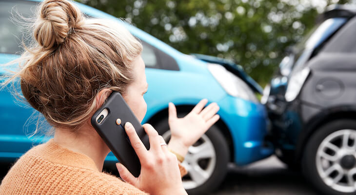 Woman talking on the phone while standing in front of a car accident