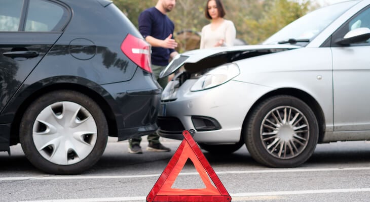 No fault insurance: warning sign and cars that crashed into each other on a road