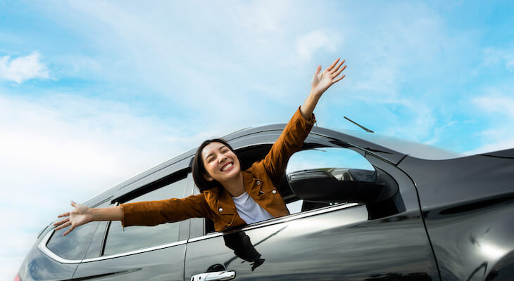Woman putting her hands up in the air while riding in a car