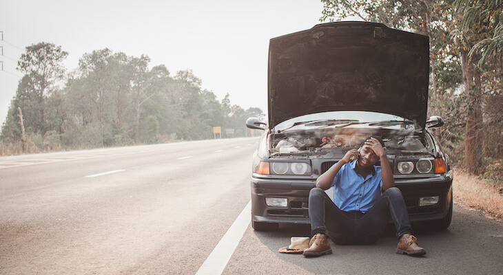 Temporary car insurance: worried man talking on the phone while sitting in front of his broken car