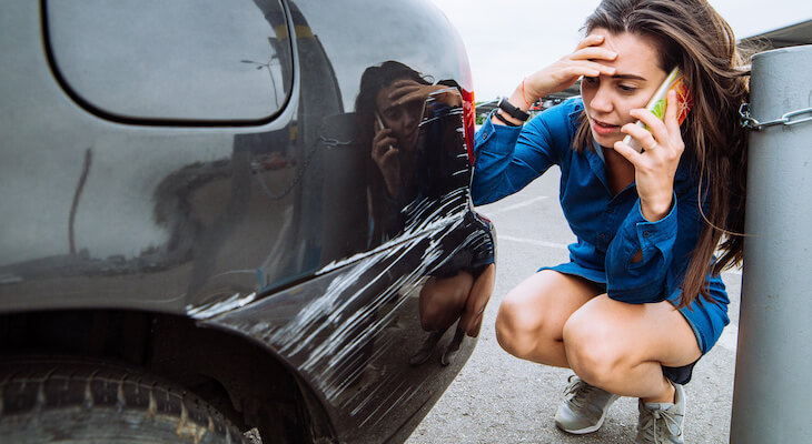 Temporary car insurance: stressed woman on the phone while looking at the scratches on her car