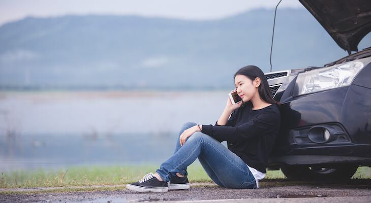 Woman sitting in front of her broken car while calling for help
