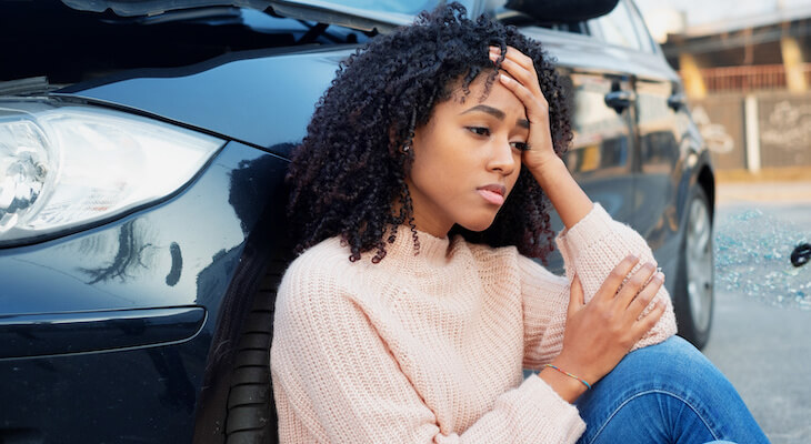 Worried woman sitting beside her car