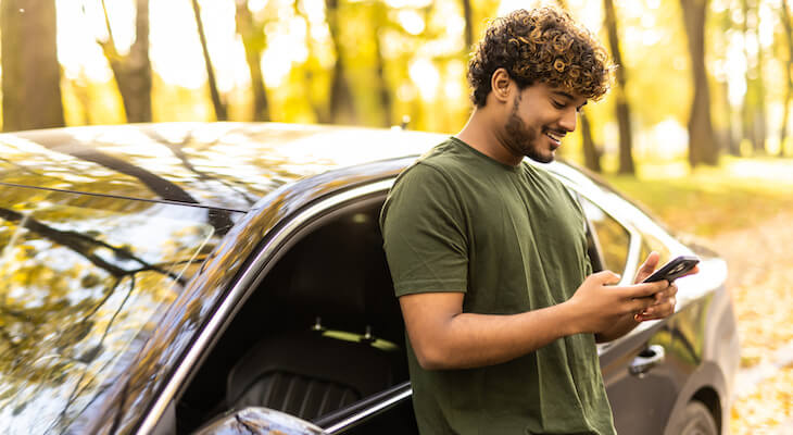 Man happily texting while standing beside his car