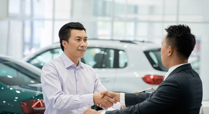 Two men shake hands in a car dealership