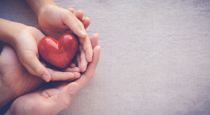 Health insurance for unemployed: an adult and a child's hands holding a red heart