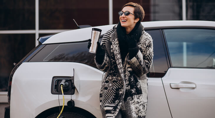 Happy woman drinking coffee while charging her car