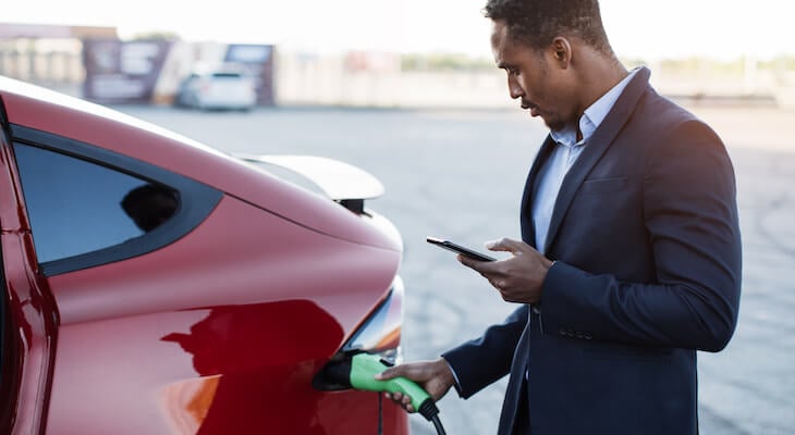 How do hybrid cars work: man holding his phone while charging his car