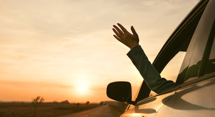 Person waving happily from the window of one of the cheapest cars to insure