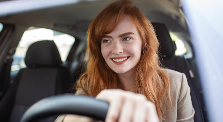 A woman happy behind the wheel driving one of the cheapest cars to insure