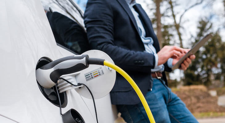Best EV charging app: man using a tablet while charging his electric car