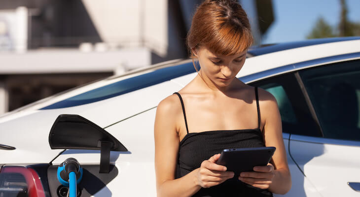 Woman using a tablet while waiting for her car to finish charging