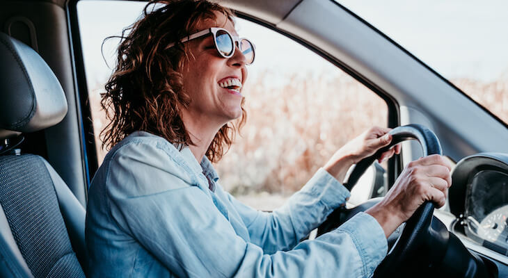 Why is my car insurance so high: woman wearing sunglasses happily driving her car