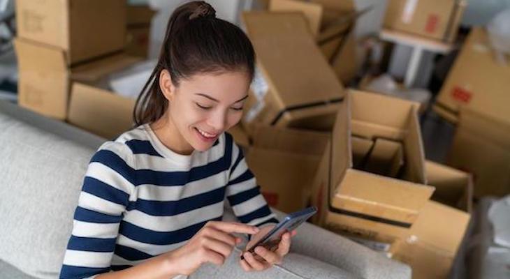 Woman happily using her phone while unpacking