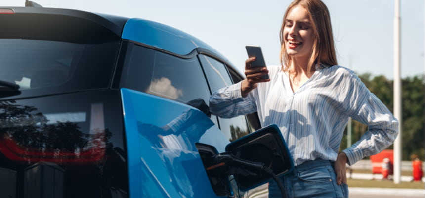 woman looking at her phone while charging her electric vehicle