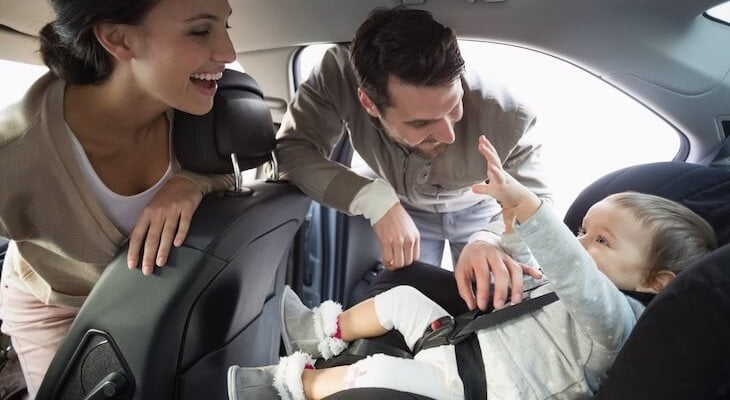 Parents securing their baby on a child safety seat