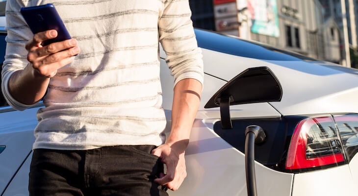 Tesla Model Y insurance cost: person checking their phone while waiting for their car to finish charging
