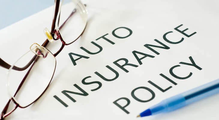 Auto Insurance Policy document, a pen and an eyeglass