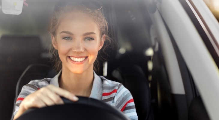 Cheapest cars to insure for young drivers: young woman smiling while driving her car
