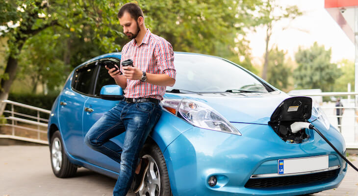 Nissan LEAF insurance cost: man using his phone while charging his car