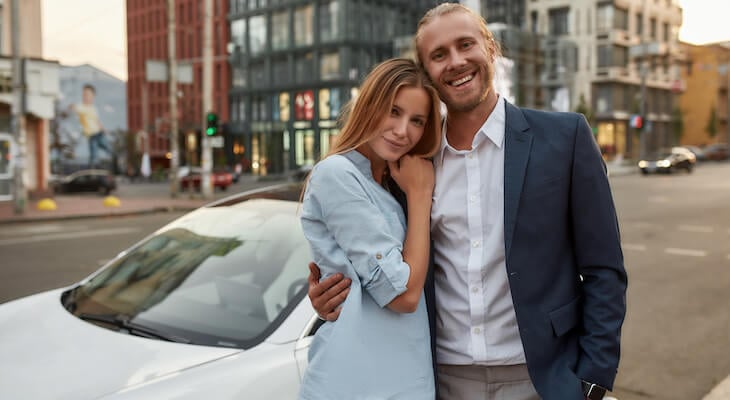 Why are electric cars so expensive: happy couple in front of their car