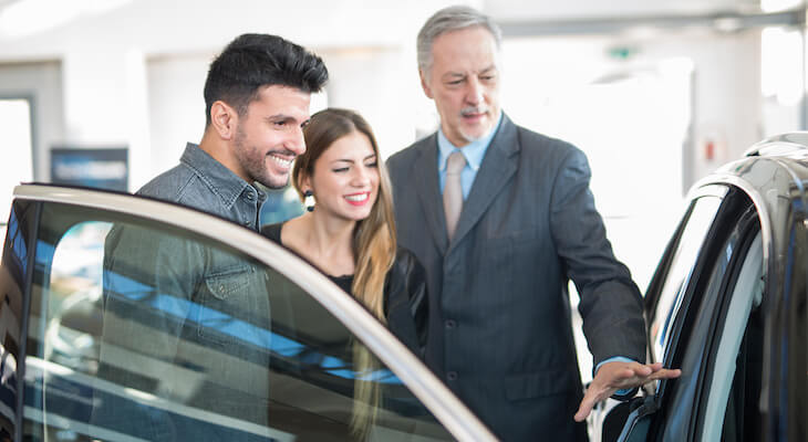 Sales person showing a car to a couple