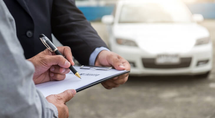 Customer signing a multi-car insurance document in front of a parked car