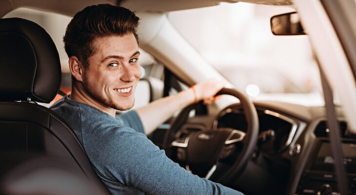 Best car insurance for young drivers: man smiling at the camera while sitting in his car