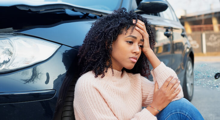 Stressed woman sitting beside her damaged car