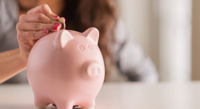 woman putting money in piggy bank that she saved on car insurance