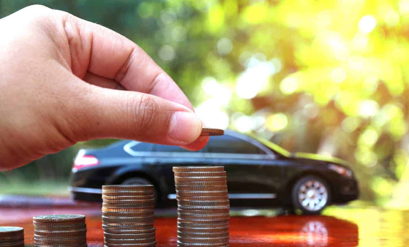 man stacking coins beside a vehicle signifying saving money on car insurance 