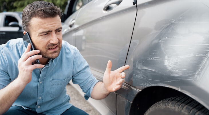 Liability vs full coverage: man talking on the phone while looking at his damaged car