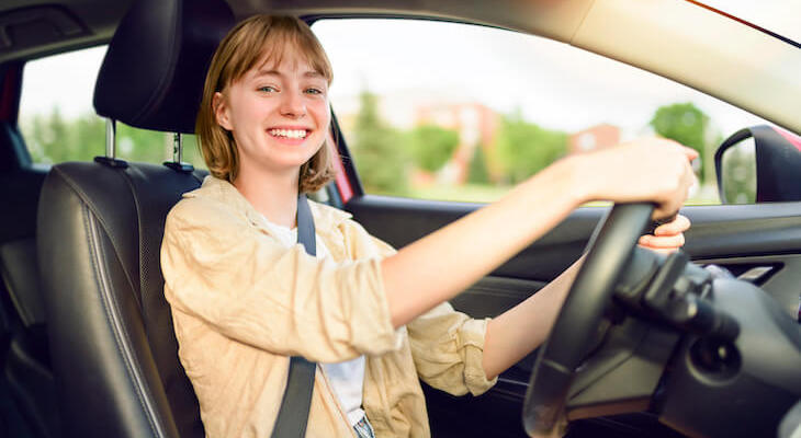 Cheapest car insurance for new drivers: young woman happily driving a car