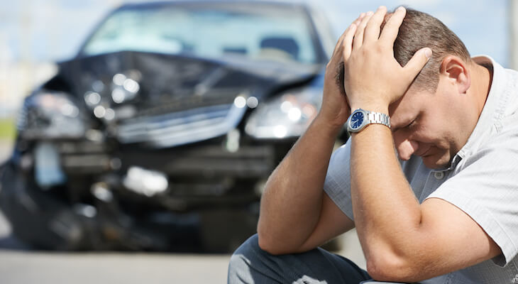 Stressed man with a damaged car in the background