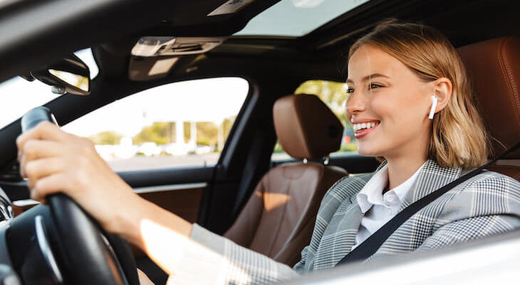 a woman happily driving her car with earbuds in, but she has the best car insurance for high-risk drivers