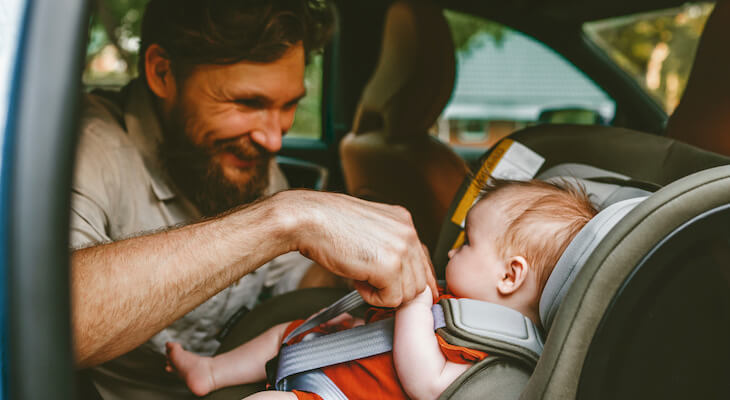 Father happily putting his baby in a child safety seat of his car