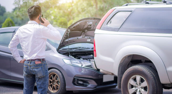 A man talking on the phone looking at an accident in need of the best car insurance for high-risk drivers