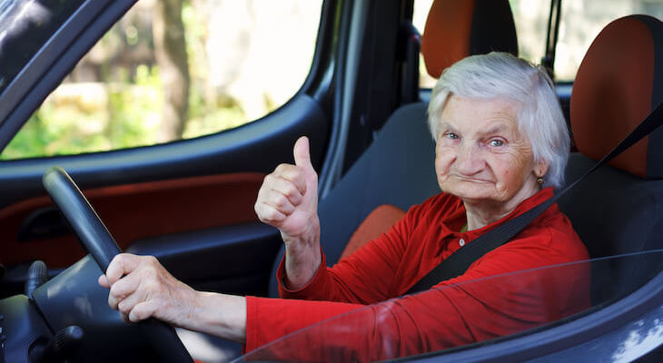 A senior woman giving the thumbs up while driving her car