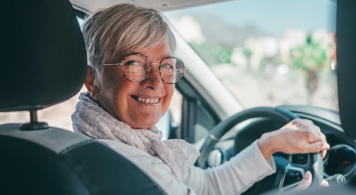 Smiling older woman behind the wheel of her car because she has the best car insurance for full coverage