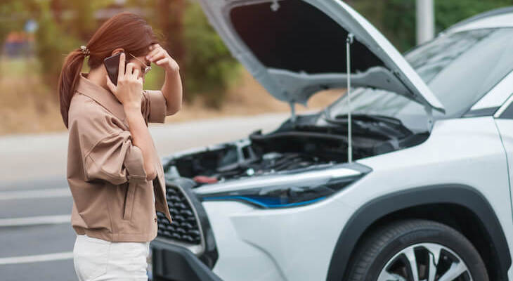 Woman talking on the phone looking under the hood of her car