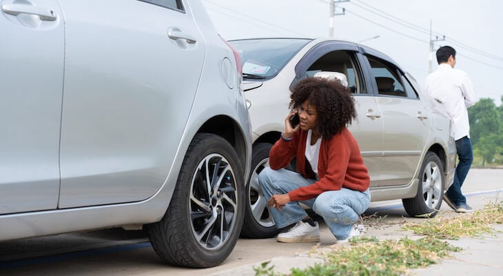 Woman talking on the phone while looking at her damaged car